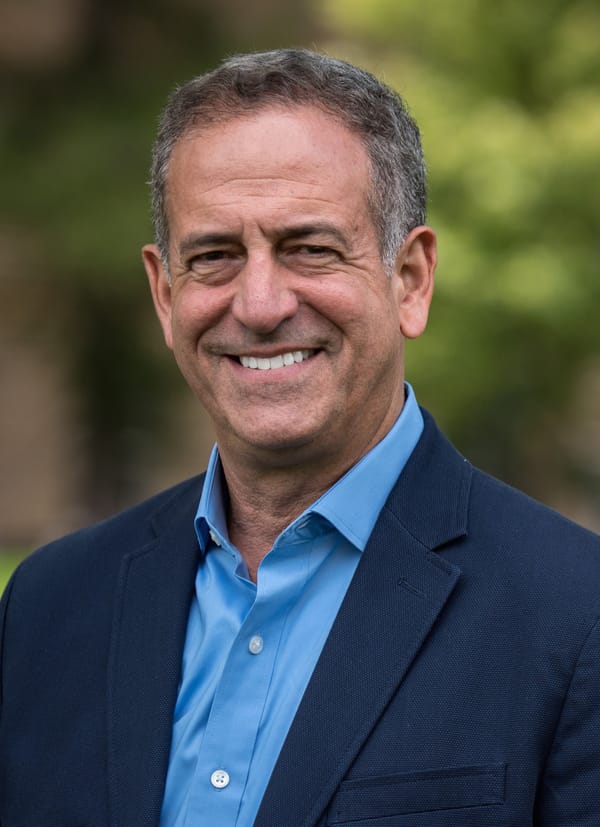 A picture of former US Senator Russ Feingold. He is wearing a blue blazer and blue dress shirt. He is smiling.